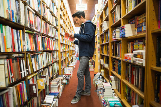 20 something man with hoody and hat browsing books at book store.