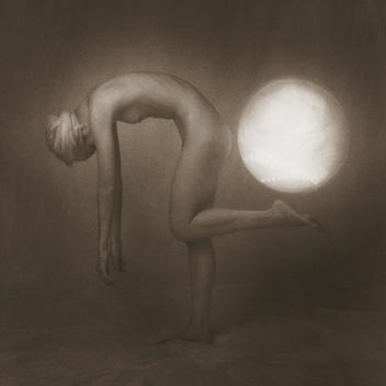 Anonymous, slender, nude woman bending from waist up with arms down and front leg uplifted as if supporting luminous lit globe