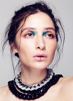 A beauty shot of a young half-Asian woman wearing a necklace and colorful make up.
