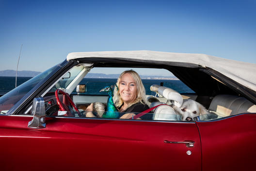 Cat Spydell in her red convertible with her pet peacock, Radagast in her lap and her dog in the backseat