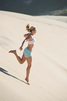 22 year old woman playing, running, jumping on giant sand dune