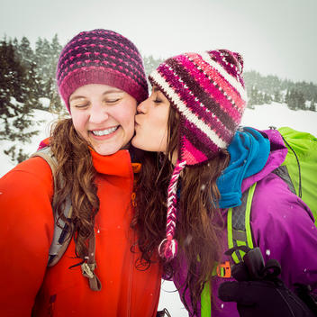 Young woman giving her friend a kiss on the cheek while taking a break from their snowshoeing adventure