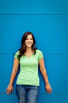 Brunette woman against a blue wall wearing a green shirt