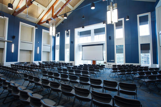 Cathedral style lecture room with rows of chairs and a projector screen.