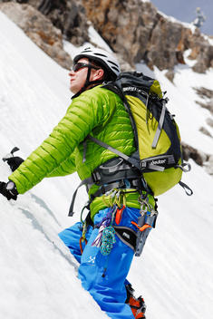 A man wearing a full tour-skiing outfit climbing in a very steep slope, snowy and mountainous landscape