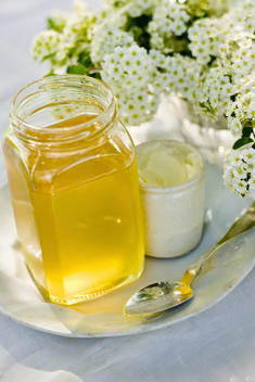 A vase of fresh flowers, a jug of cream and a pot of honey on a table.