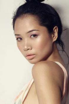 Young Asian girl portrait, wearing soft pink make up, hair up in a bun, looking at the lens