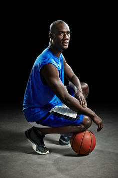 Studio portrait of basketball player kneeling on ball