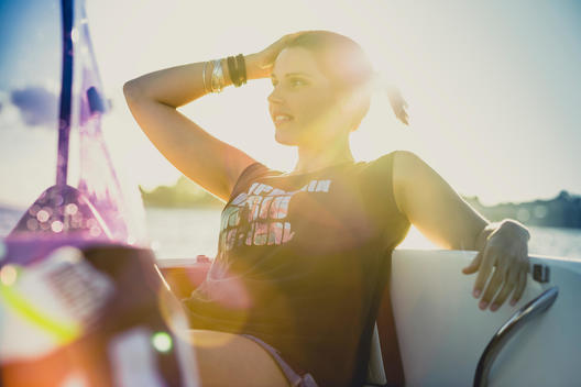 young woman wearing a fashionable outfit while sitting on a boat at summer and looking into the distance, back light and lens flare
