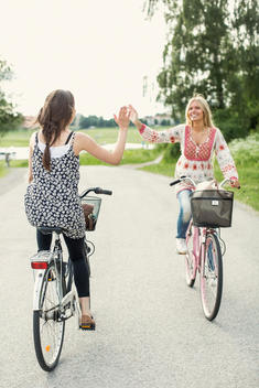 Happy female friends giving high five while cycling on country road