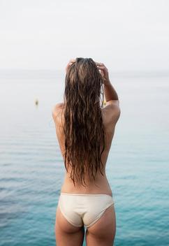 Rear view of young woman wearing bikini bottoms with hands in hair at coast