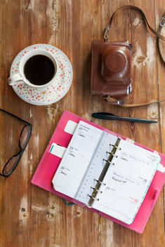 Directly above shot of open diary with glasses, coffee, pen and camera on wooden table