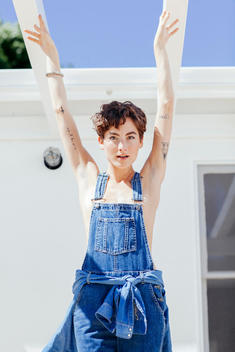Attractive women with short hair holding her hands in the air, wearing denim overalls.
