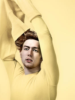ginger haired boy taking ayellow jumper off with messy hair and yellow background
