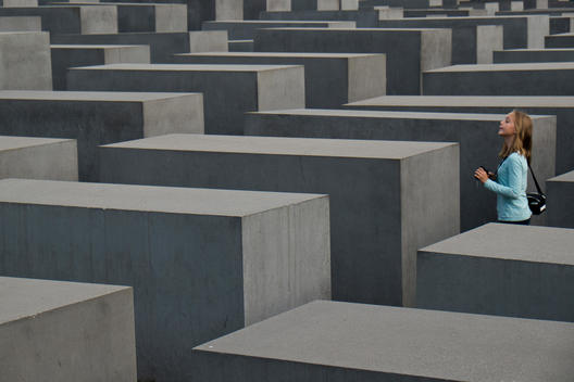 The Holocaust Memorial designed by the architect Peter Eisenman. A girl looking and standing on one of the paths between the grey concrete steal blocks.