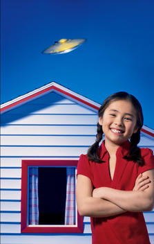 Smiling girl standing in front of her house with a flying saucer in the background