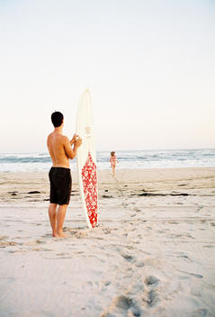Young Man With Surfboard On Beach With Woman