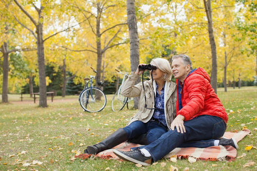 Full length of mature man with woman looking through binoculars at park