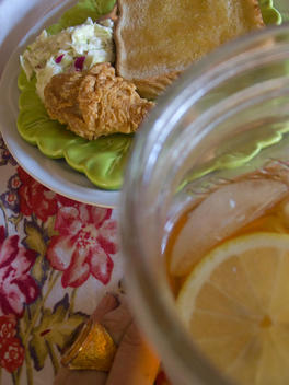 Southern Style Picnic Dinner Of Fried Chicken, Texas Toast, Cole Slaw And Sweet Tea On A Table Top With A Floral Tablecloth. A Woman Wearing A Cocktail Ring Is Holding The Glass Of Tea.