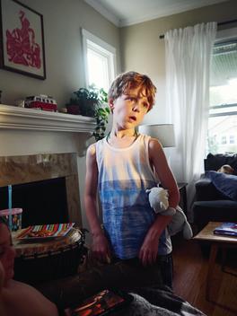 Boy with blue bear and tank top inside house on a summer morning.