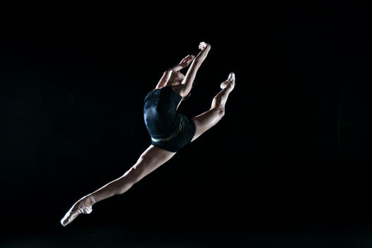 A ballerina Leaping against a black backdrop looking athletic.