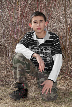 A Portrait Of A Boy In Camouflage In The Woods By His House.