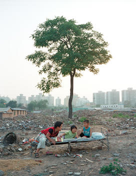 Three children lying on a cot in front of a tree in area slated for construction in North Beijing, China, 2005.