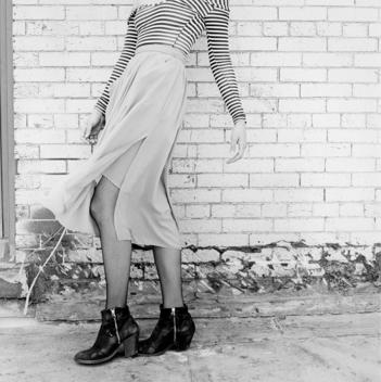 Detail of young ethnic Asian Chinese-American woman's tight striped top, wind-blown skirt, and heels against a white brick wall. New York, NY