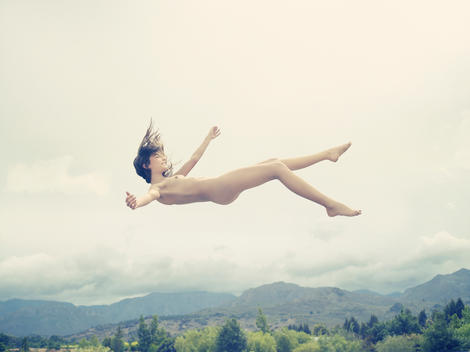 Girl Floating In The Air With Sky, Mountains And Trees In The Background.