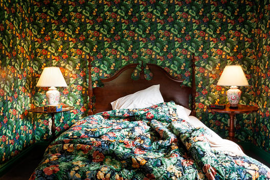 Green flowered wallpaper bedroom and un made bed.