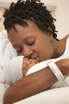 Black woman kissing newborn baby in hospital bed