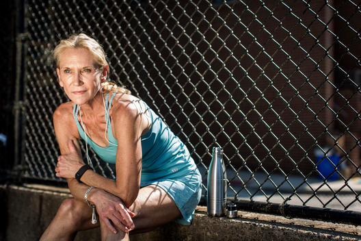 Portrait of an older 50-plus woman resting near a fence after her workout.