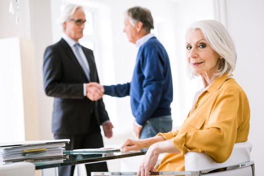 Senior woman in business meeting looking over shoulder at camera smiling