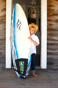 boy on a porch deck with surf board and cowboy hat