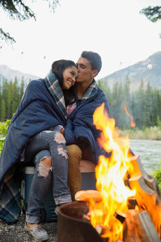 Couple wrapped in blanket hugging at campfire
