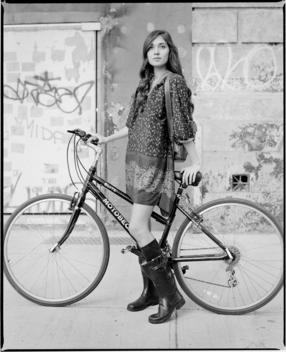 A Young European Woman Rides Her Bicycle In Front Of A Run-Down Dilapidated Building With Graffiti Near Union Square During A Fashion Shoot For Clothing Brand Callalilai. New York City.
