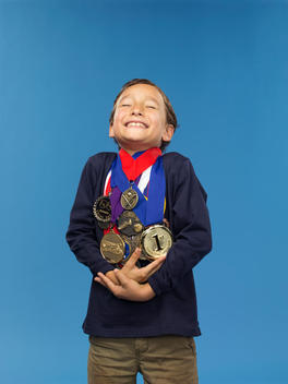 A boy smiles as he clutches at the many medals hanging around his neck