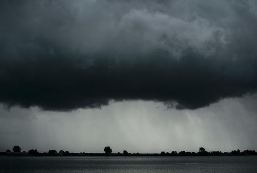 Black and white image of heavy rainfall over lake during thunderstorm