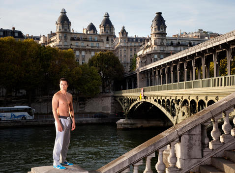 Portrait of athletic man standing on stone wall, shirtless, in European urban setting
