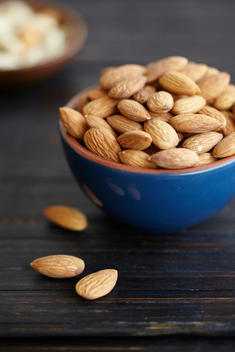 Whole Almonds In Blue Terra Cotta Bowl And Scattered On Rustic Wood Table.