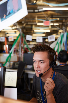 A young male employee at the Zappos company speaks on a headset at his desk
