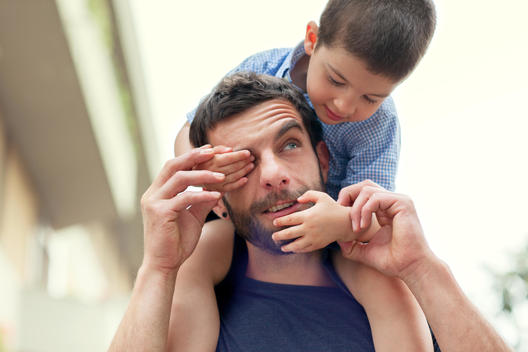 Father carrying son on shoulders, boy covering man\'s eye