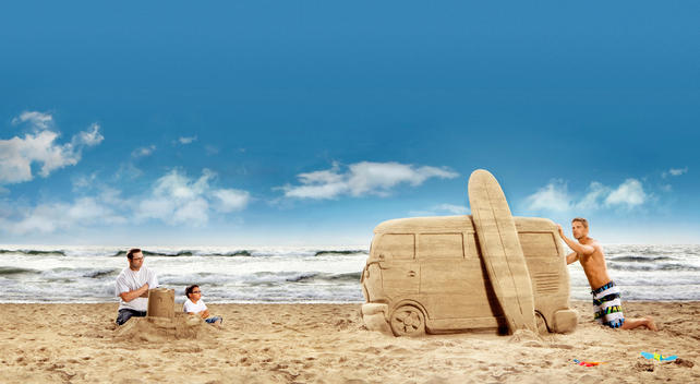 Father and son sitting with their sand castle staring at man making a sand castle van
