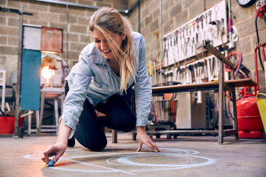 A talented female glassblower sketches out her design on the floor of her glassblowing studio in London