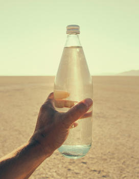 The Landscape Of The Black Rock Desert In Nevada. A Man\'S Hand Holding A Bottle Of Water. Filtered Mineral Water.