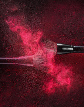 Cosmetic brushes colliding creating a red powder explosion mimicking a galaxy