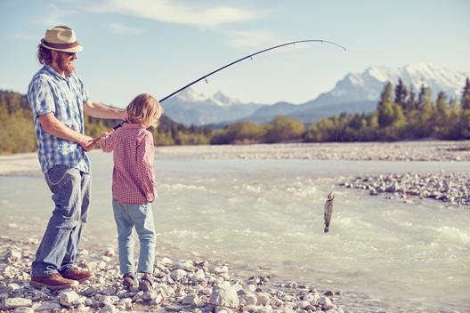Mid adult man and boy near river holding fishing rod with fish attached, Wallgau, Bavaria, Germany