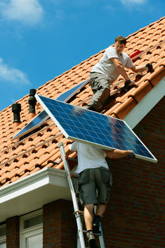 Workers carrying and installing solar panels on roof of new home, Netherlands