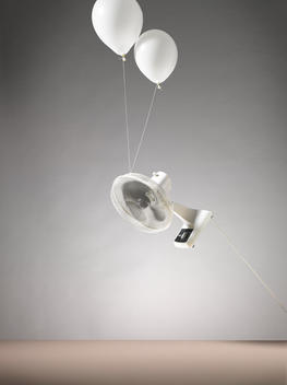 An Oscillating Desk Fan Being Lifted In The Air By Two Balloons
