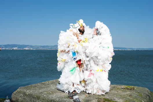 A man and woman covered in plastic bags stand together on a rock in front of the ocean